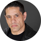 The image features a focused individual with a strong expression, wearing a black leather jacket against a neutral background.